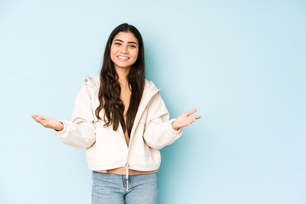 Young indian woman on blue showing a welcome expression.