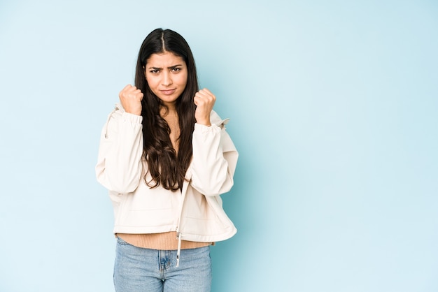 Young indian woman on blue wall showing fist , aggressive facial expression.