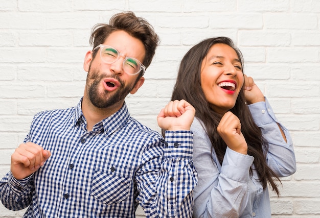 Young indian woman and caucasian man couple listening to music, dancing and having fun, moving, shouting and expressing happiness, freedom concept