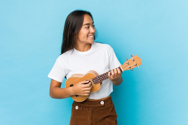 Ukelele di gioco felice della giovane donna indiana isolato