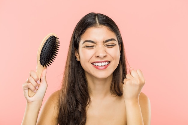 Young indian woman holding a hairbrush cheering carefree and excited.