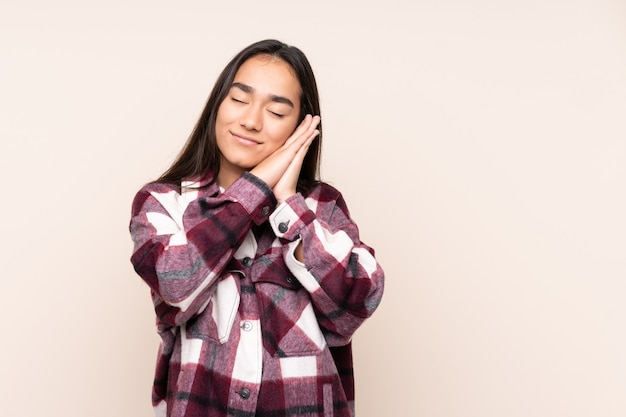 Young Indian woman isolated on beige background making sleep gesture in dorable expression