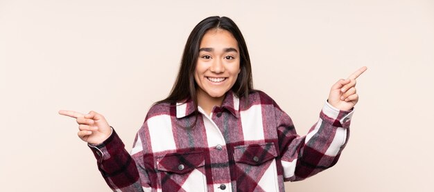 Young Indian woman isolated on beige background pointing finger to the laterals and happy