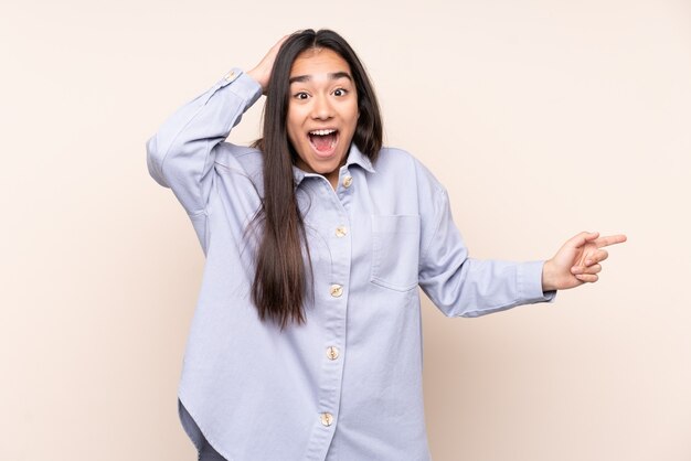 Young Indian woman isolated on beige background surprised and pointing finger to the side