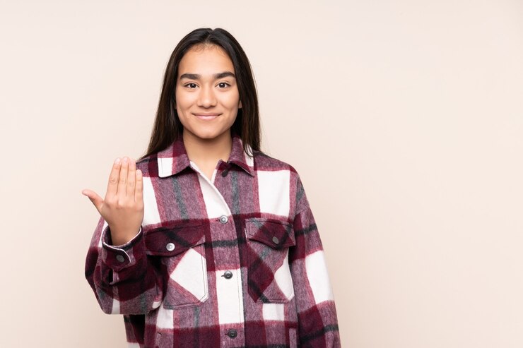 Photo young indian woman isolated on beige inviting to come with hand. happy that you came