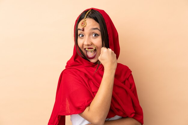 Young Indian woman isolated on beige wall celebrating a victory