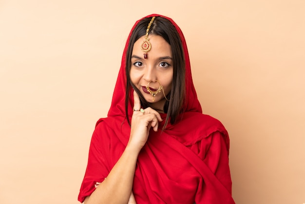 Young Indian woman isolated on beige wall and thinking