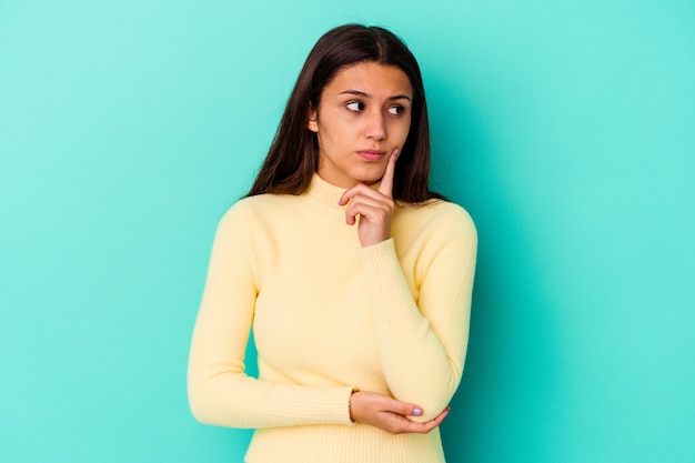 Young Indian woman isolated on blue background contemplating, planning a strategy, thinking about the way of a business.