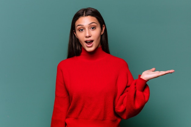 Young Indian woman isolated on blue background impressed holding copy space on palm.