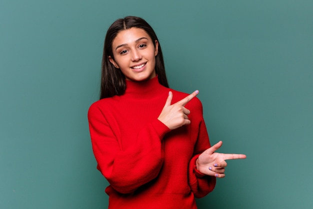 Young Indian woman isolated on blue excited pointing with forefingers away.