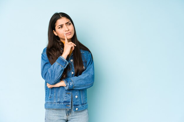 Giovane donna indiana isolata sull'azzurro che guarda lateralmente con espressione dubbiosa e scettica.