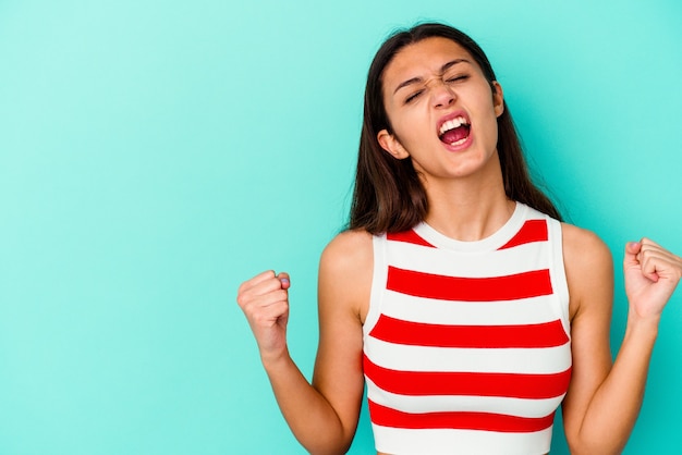 Young Indian woman isolated on blue raising fist after a victory, winner concept.