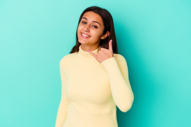 Young Indian woman isolated on blue showing a mobile phone call gesture with fingers.