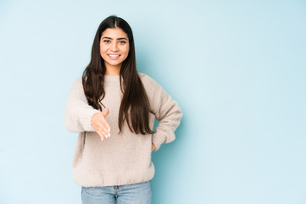 Young indian woman isolated on blue stretching hand in greeting gesture.