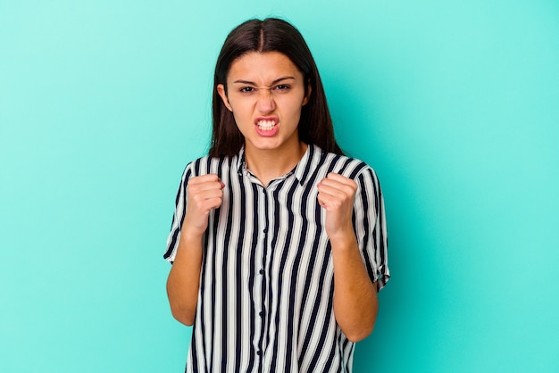 Young Indian woman isolated on blue upset screaming with tense hands.