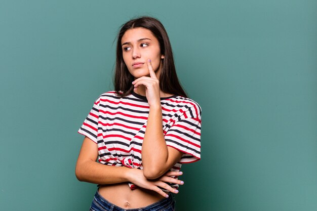 Young Indian woman isolated on blue wall contemplating, planning a strategy, thinking about the way of a business.