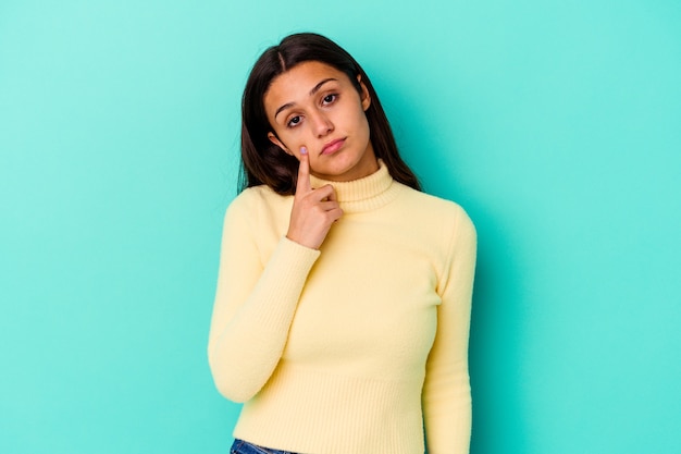 Young Indian woman isolated on blue wall crying, unhappy with something, agony and confusion concept.