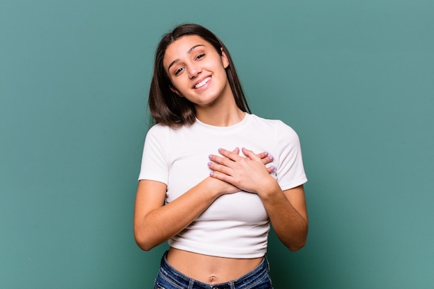 Young Indian woman isolated on blue wall has friendly expression, pressing palm to chest. Love concept