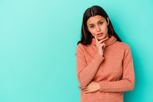 Young Indian woman isolated on blue wall looking sideways with doubtful and skeptical expression.