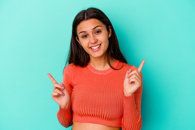 Young Indian woman isolated on blue wall pointing to different copy spaces, choosing one of them, showing with finger.