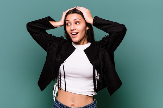 Young Indian woman isolated on blue wall screaming, very excited, passionate, satisfied with something.