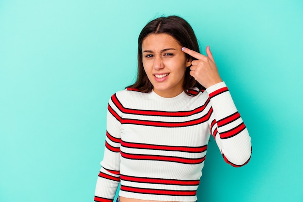 Young Indian woman isolated on blue wall showing a disappointment gesture with forefinger.