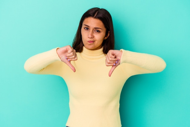 Young Indian woman isolated on blue wall showing thumb down, disappointment concept.