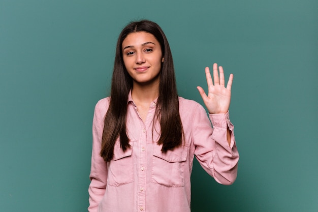 Young Indian woman isolated on blue wall smiling cheerful showing number five with fingers.