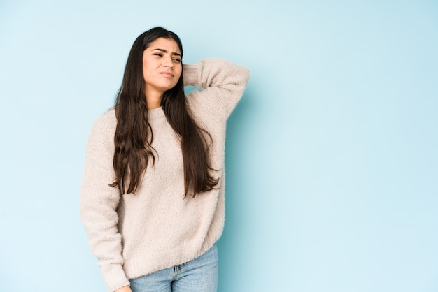 Young indian woman isolated on blue wall tired and very sleepy keeping hand on head.