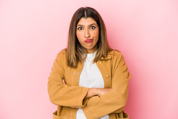 Young indian woman isolated on pink background blows cheeks, has tired expression. facial expression concept