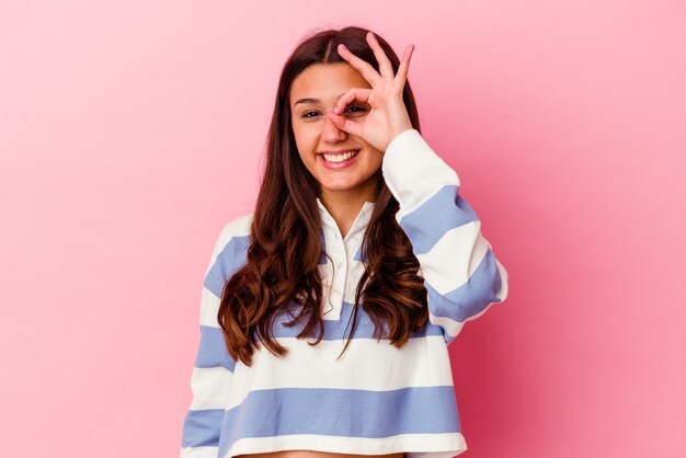 Young Indian woman isolated on pink background excited keeping ok gesture on eye.