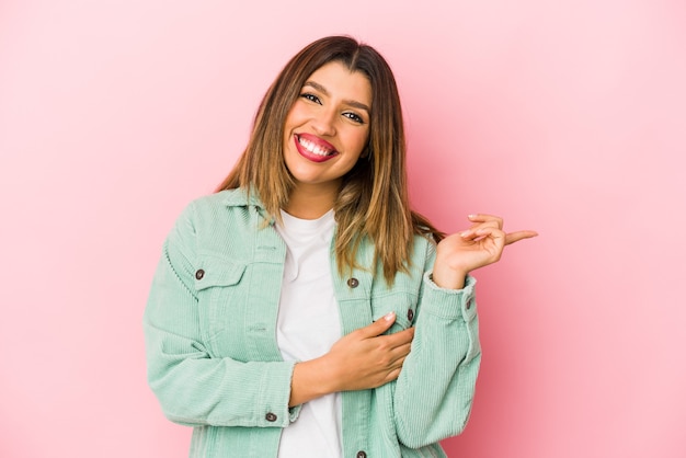 Young indian woman isolated on pink background smiling cheerfully pointing with forefinger away.