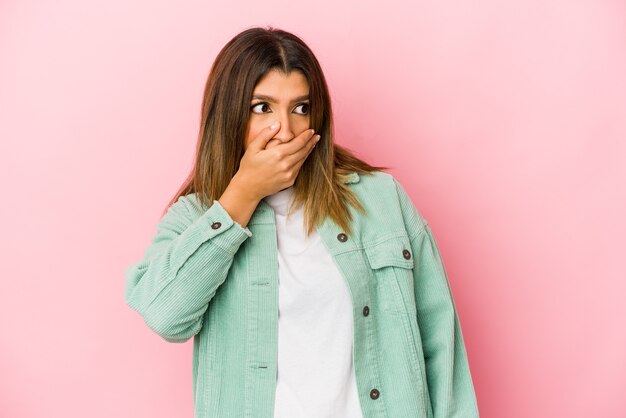 Photo young indian woman isolated on pink space thoughtful looking to a copy space covering mouth with hand.