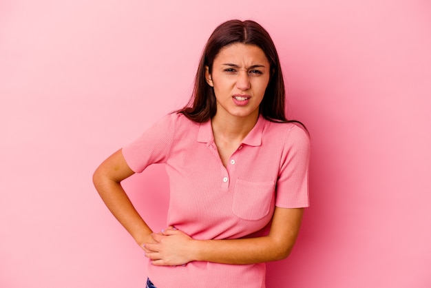 Young Indian woman isolated on pink wall having a liver pain, stomach ache.