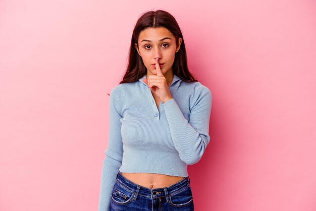 Young Indian woman isolated on pink wall keeping a secret or asking for silence.