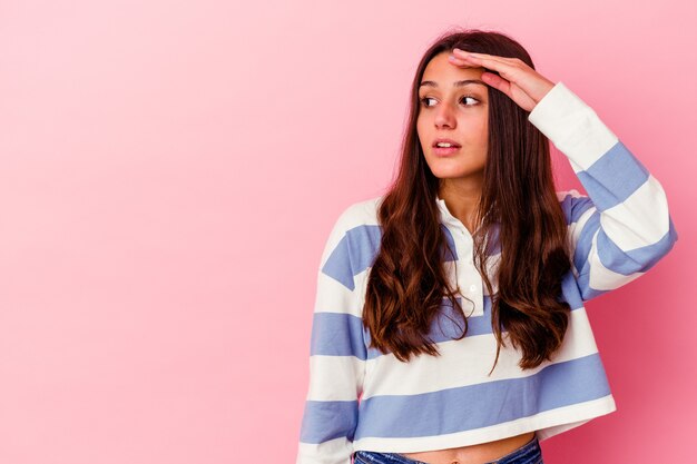 Young Indian woman isolated on pink wall looking far away keeping hand on forehead.