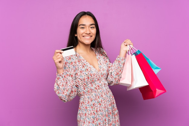 ショッピングバッグとクレジットカードを保持している紫色の背景で隔離の若いインド人女性