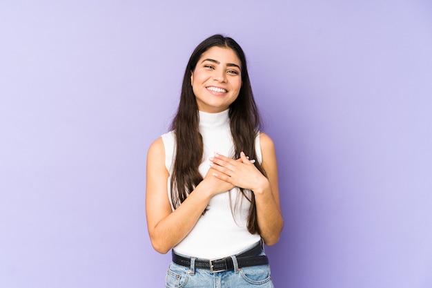 Young indian woman isolated on purple background laughing keeping hands on heart, concept of happiness.