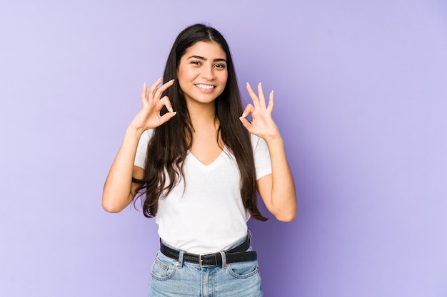 Young indian woman isolated on purple wall cheerful and confident showing ok gesture.