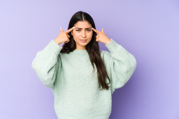 Young indian woman isolated on purple wall focused on a task, keeping forefingers pointing head.