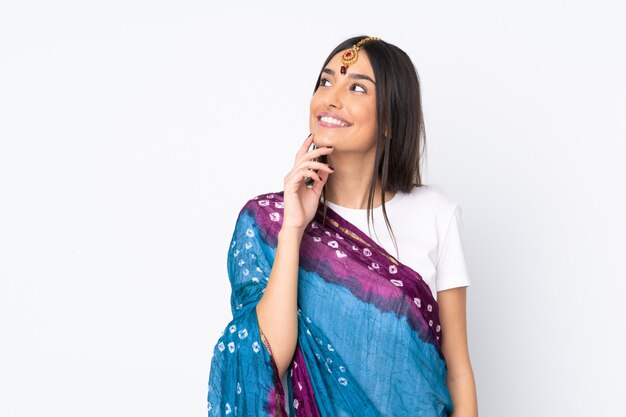 Young Indian woman isolated on white wall thinking an idea while looking up