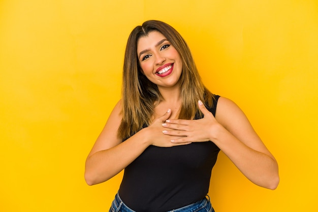 Young indian woman isolated on yellow background has friendly expression, pressing palm to chest. Love concept.