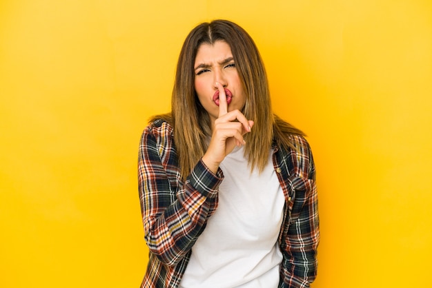 Giovane donna indiana isolata su sfondo giallo mantenendo un segreto o chiedendo il silenzio.