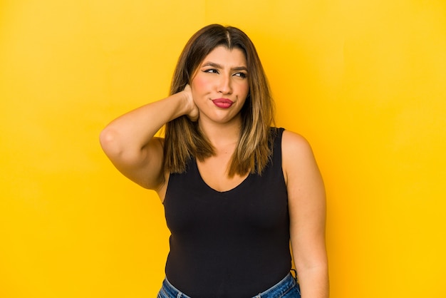 Young indian woman isolated on yellow background touching back of head, thinking and making a choice