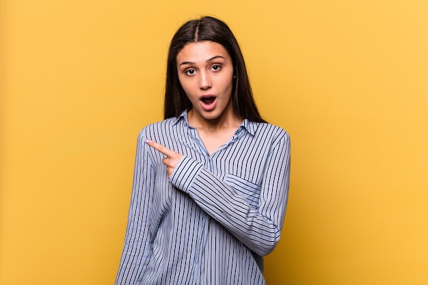 Young Indian woman isolated on yellow pointing to the side