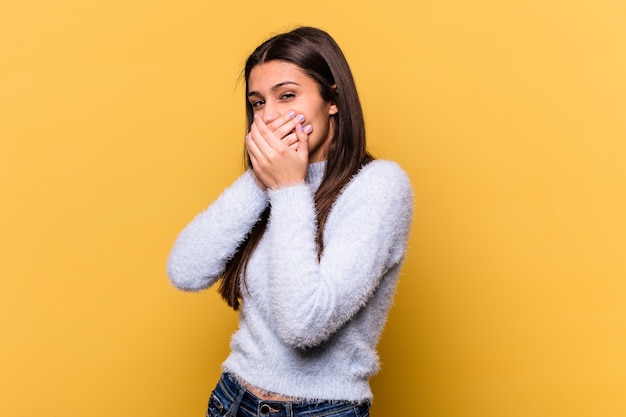 Young Indian woman isolated on yellow wall covering mouth with hands looking worried.