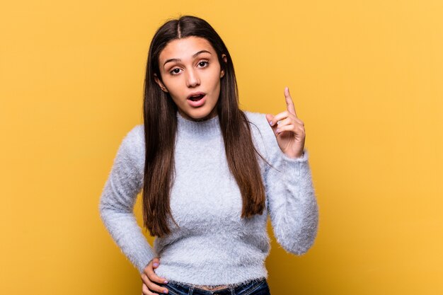 Young Indian woman isolated on yellow wall having an idea, inspiration concept.