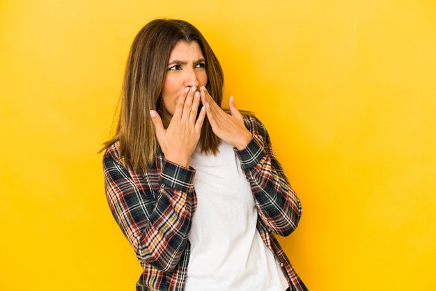 Young indian woman isolated on yellow wall laughing about something, covering mouth with hands.