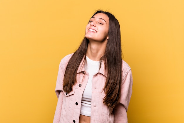 Young Indian woman isolated on yellow wall relaxed and happy laughing, neck stretched showing teeth