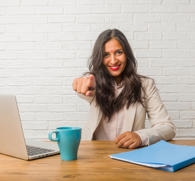 Young indian woman at the office cheerful and smiling pointing to the front